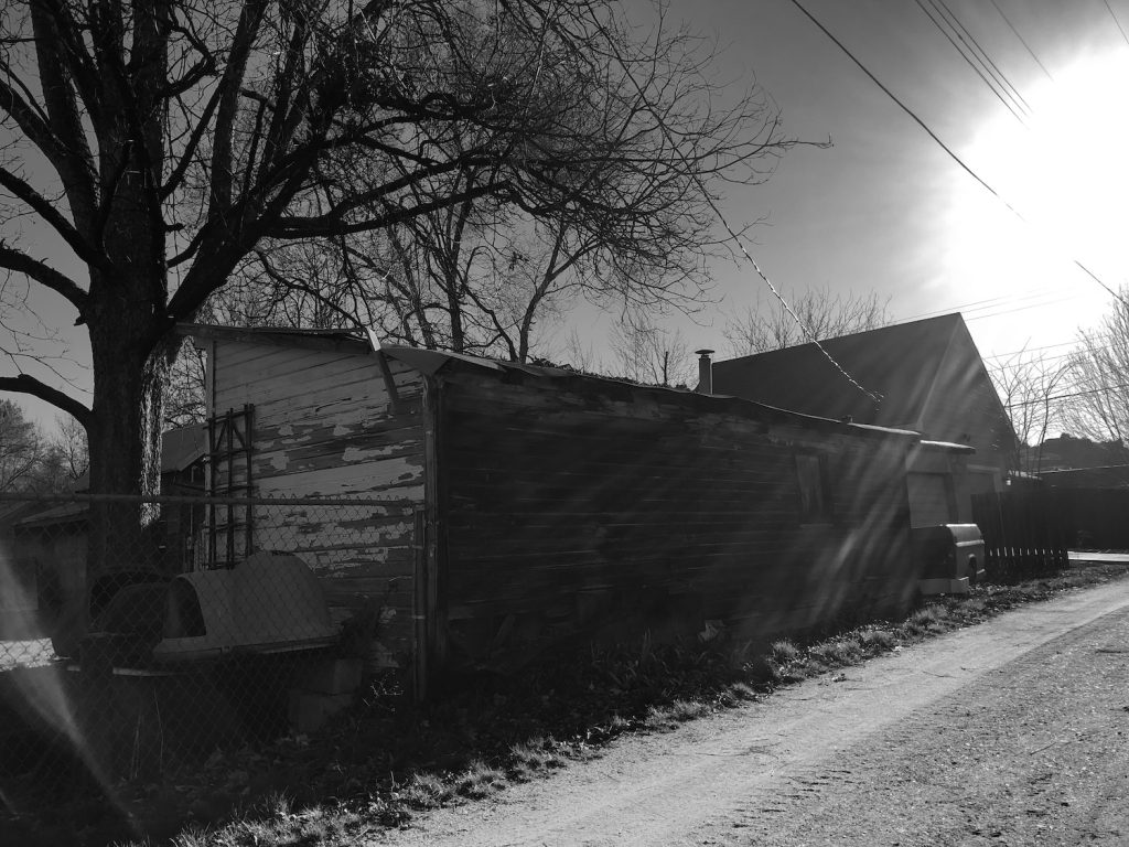 black and white photo of alley and old outbuildings with distorted sunlight